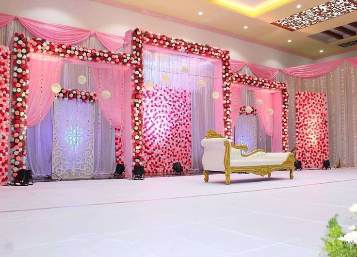 Birthday party stage decorated with pink drapes, floral arrangements, and warm lighting, featuring a golden couch as the centerpiece for the celebration.